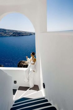 a woman sitting on the edge of a building looking out at the water and blue sky