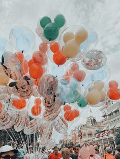 a bunch of balloons with mickey mouse heads on them are being held up by people