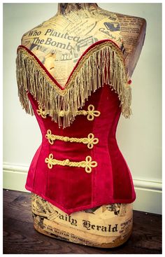 a red corset with fringes and buttons on the back is sitting on a wooden table