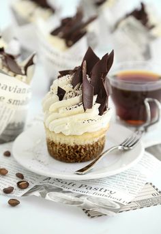 cupcakes with white frosting and chocolate decorations on a plate next to coffee