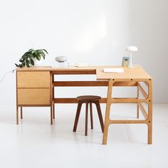 a wooden desk with a plant on top and a chair next to it, in front of a white wall