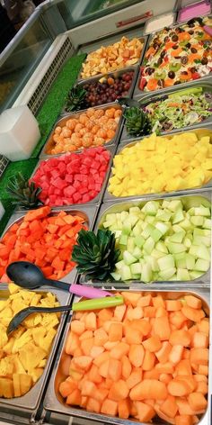 an assortment of fruits and vegetables on display in trays at a buffet table with utensils