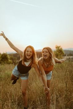 two young women are playing in the tall grass with their arms up and legs spread out