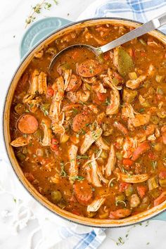 a pot filled with chicken and vegetable soup on top of a white table cloth next to a spoon