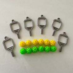 six plastic balls and two metal hooks on a white surface with one yellow ball in the middle