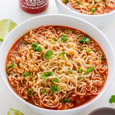 two bowls filled with noodles and garnished with cilantro on the side