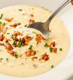 a white bowl filled with soup topped with bacon and green onions next to a spoon