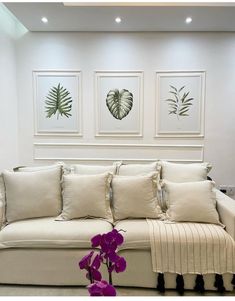 a living room with white couches and paintings on the wall above them, along with a purple flower