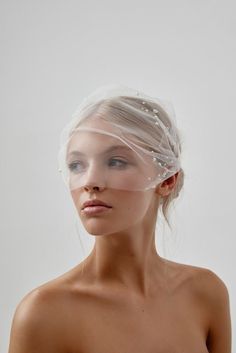 a woman with clear plastic covering her head and shoulders, looking at the camera while standing in front of a white background