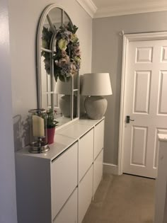 a white dresser topped with a mirror next to a lamp and vase filled with flowers