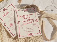 two wedding cards sitting on top of a table next to wine glasses and other items