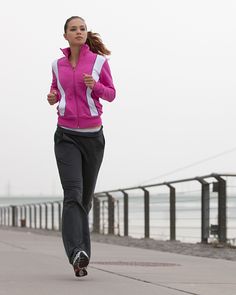 a woman running down a sidewalk next to the ocean with her cell phone up to her ear