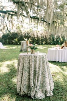 a table with flowers and candles on it in the middle of a grassy area surrounded by trees