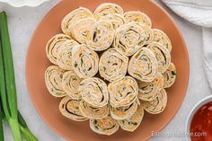 a plate filled with rolled up sandwiches next to green onions