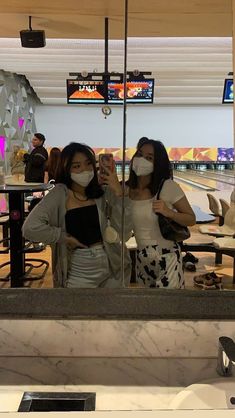 two women wearing face masks standing in front of a bowling alley