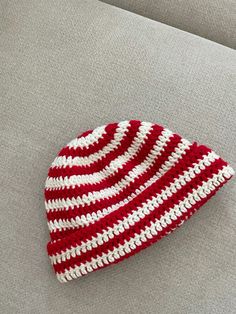 a red and white crocheted beanie sitting on top of a gray couch