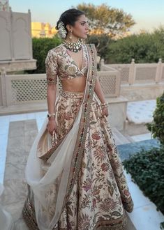 a woman in a white and gold lehenga is standing on the steps outside