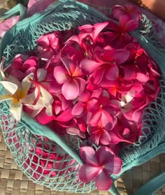 pink and white flowers are in a blue bag on a woven tablecloth with a person's hand