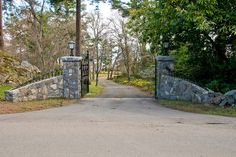 a gated entrance to a wooded area with stone walls and gates on either side