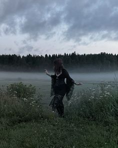 a woman is walking in the grass with her arms outstretched