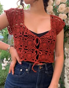 a woman wearing a red crochet top standing next to a flower covered wall