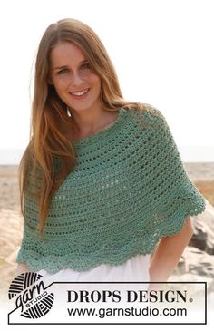 a woman wearing a green crocheted shawl on top of a sandy beach