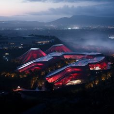 an aerial view of a building lit up in red at night with fog coming off the ground