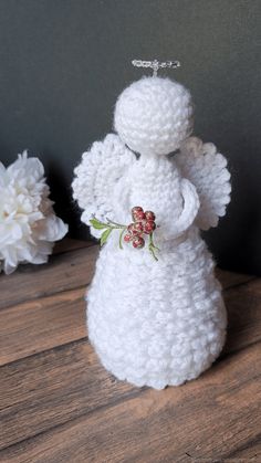 a crocheted angel figurine sitting on top of a wooden table next to white flowers