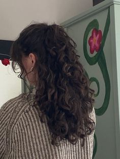 a woman with curly hair standing in front of a mirror and painting on the wall