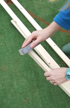 a person holding a piece of wood in their hand while standing next to a fence