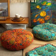 three brightly colored poufles sit on the floor in front of paintings and artwork