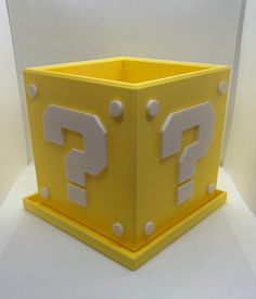 a yellow box with question marks on the front and sides, sitting on a white surface