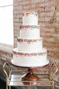 a white cake with sprinkles sitting on top of a metal rack next to a brick wall