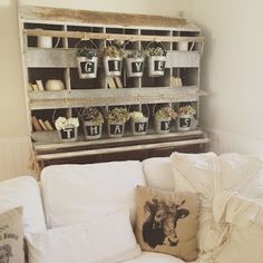 a living room filled with white furniture and lots of plants on the shelf above it