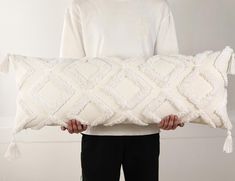 a person holding a large white pillow with tassels on the bottom and sides