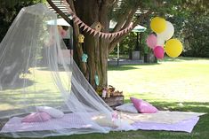 a bed with a net and balloons hanging from it's side in front of a tree