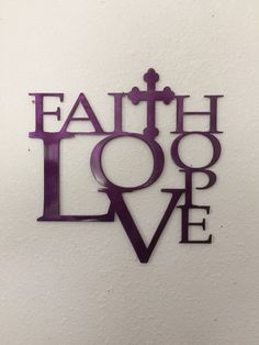 the word faith love is made up of metal letters and purple lettering on a white wall