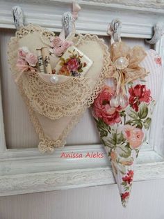 two heart shaped items hanging on a white wall next to a frame with lace and flowers