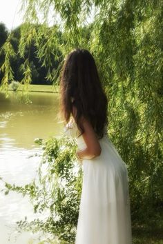 a woman in a white dress is standing by the water