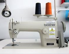 a white sewing machine with three spools of thread on the table next to it