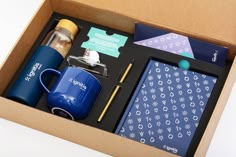 an open box with items in it including a coffee mug, notepad and pen