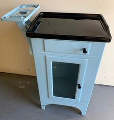 a small white cabinet with black top and drawer on the bottom, next to a wall