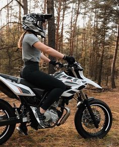 a woman riding on the back of a white motorcycle in front of a forest filled with trees