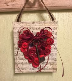 a heart made out of buttons with a key hanging from it's side on a wall