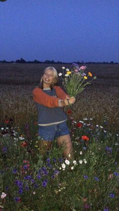 a woman is holding flowers in a field at night with the moon shining behind her