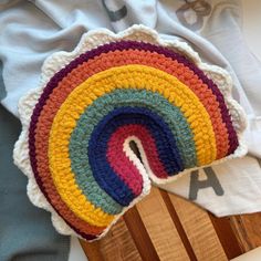 a crocheted rainbow rug sitting on top of a wooden chair next to a white t - shirt