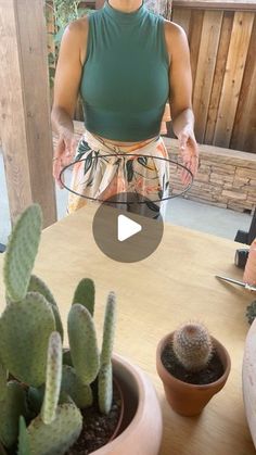 a woman standing in front of a wooden table with two cacti on it