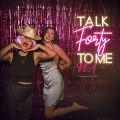 two women are posing for a photo in front of a neon sign that says talk tooty to me