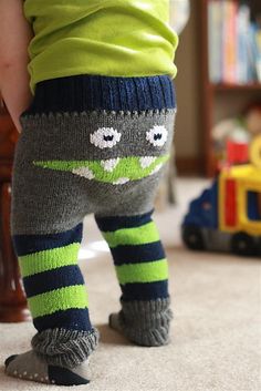 the legs of a child wearing green and blue striped socks with eyes on them, standing in front of a toy train