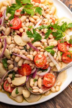 a white plate topped with beans, tomatoes and parsley on top of a wooden table